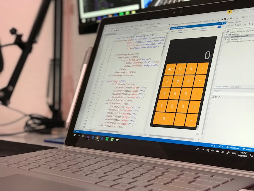 A close-up view of a laptop with a white body, open on a desk displaying a coding interface with HTML and CSS code visible on the screen. To the right of the code, there is a calculator application wi